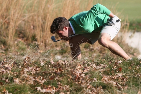 Golfer searching through leaves for golf ball
