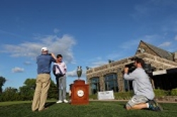 Golfer receiving award with photographer nearby.