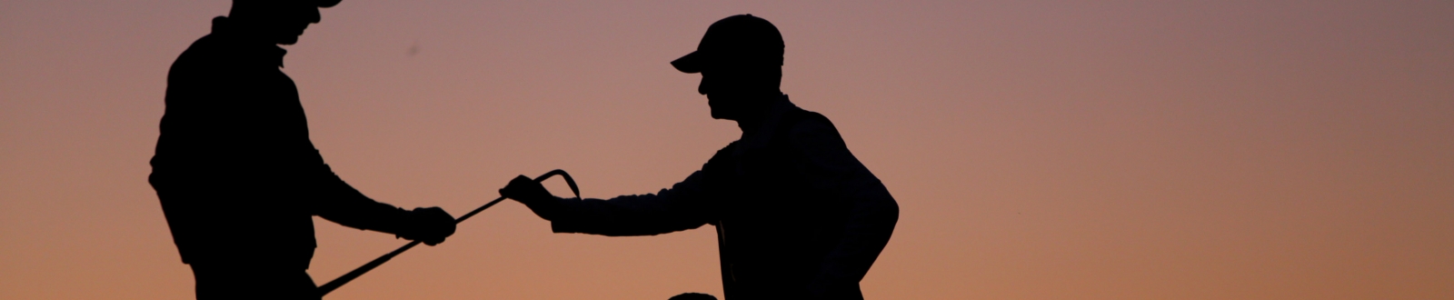 Caddie handing a golfer a club at dusk